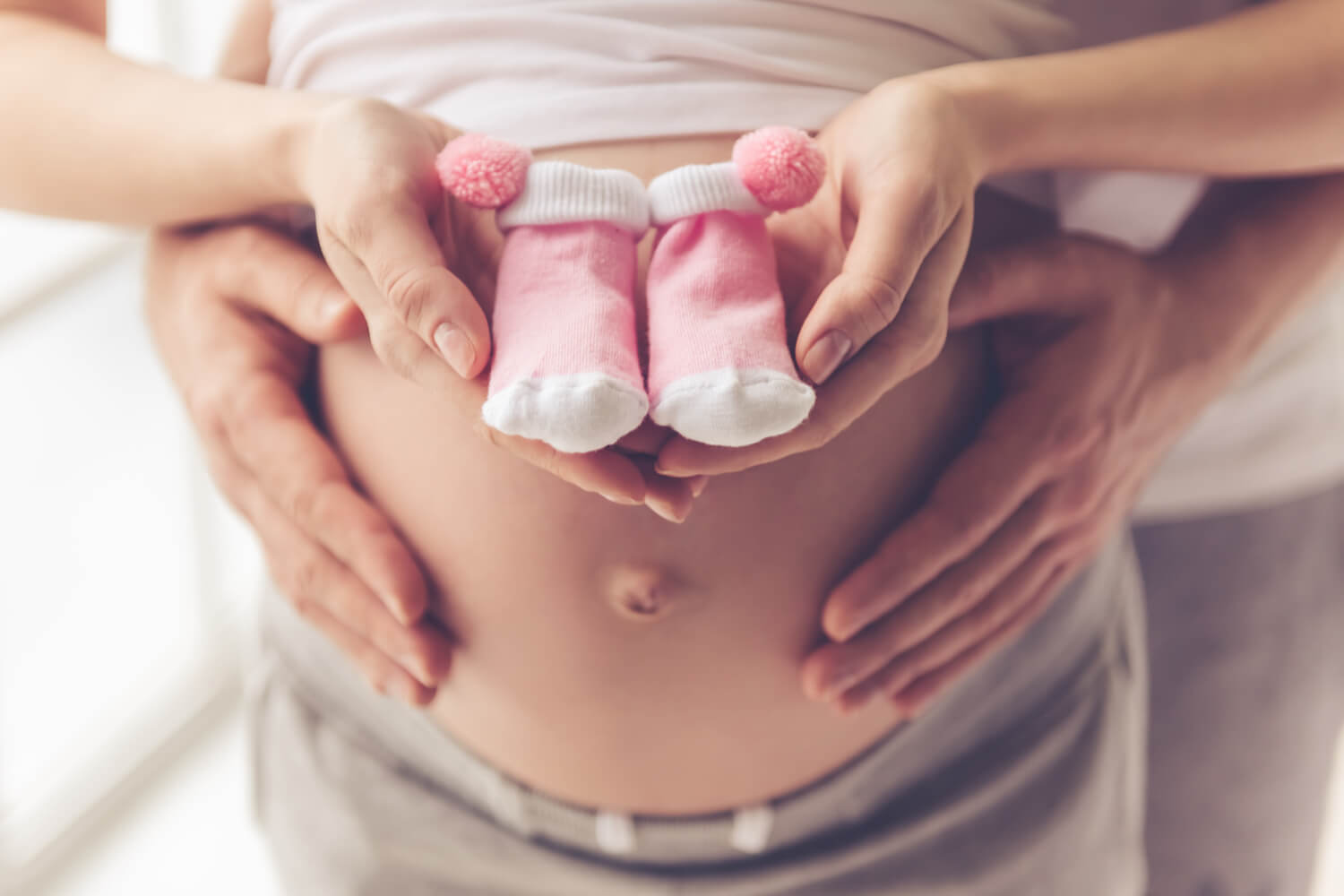 pregnant woman and her husband holding baby shoes and hugging the tummy