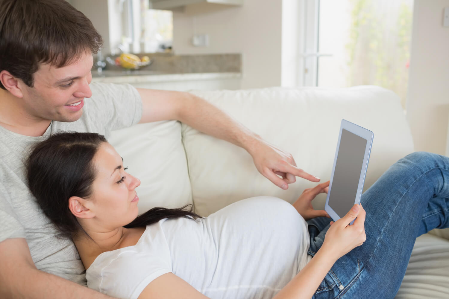 happy pregnant woman with husband looking tab