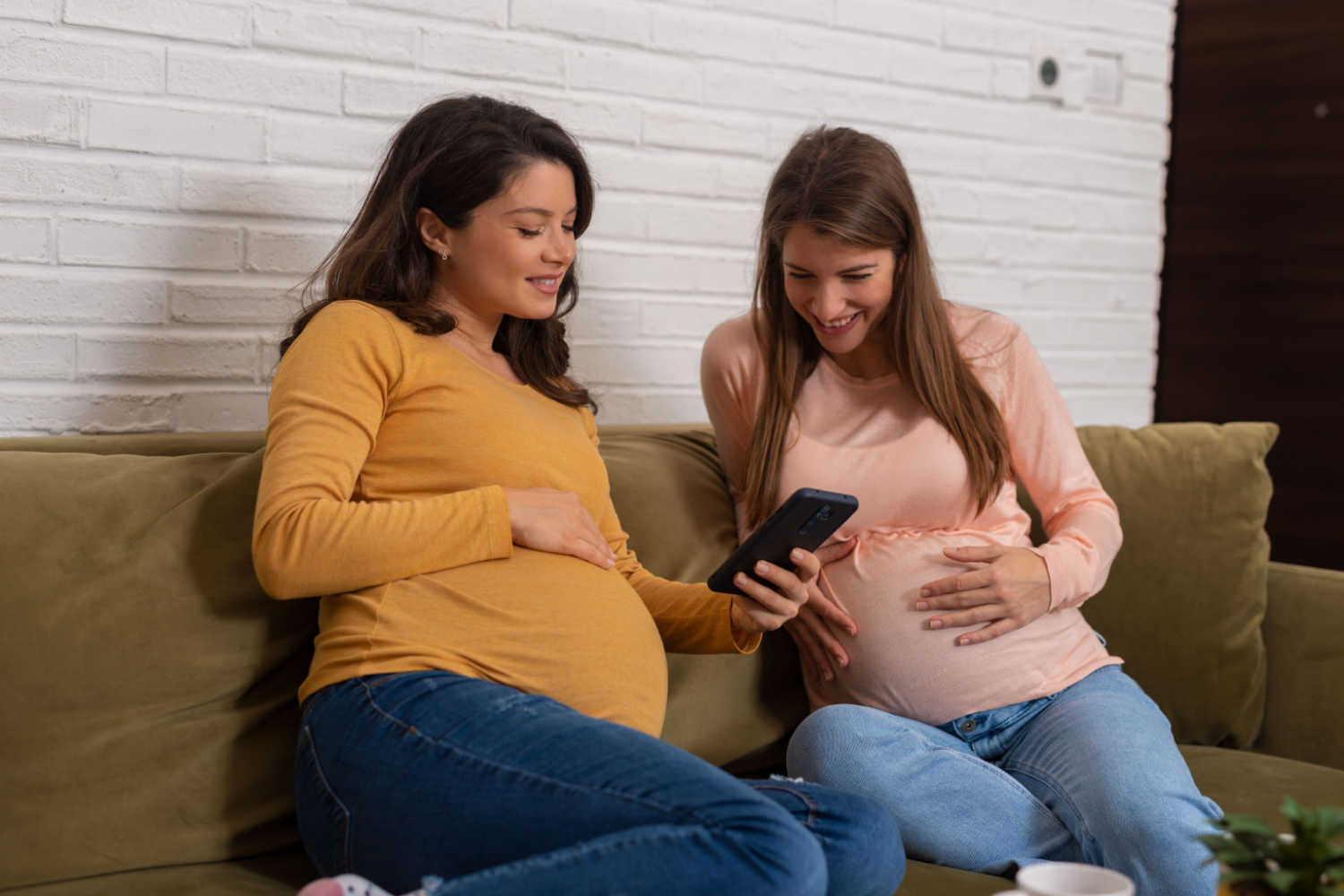 two pregnant women looking at phone and smiling