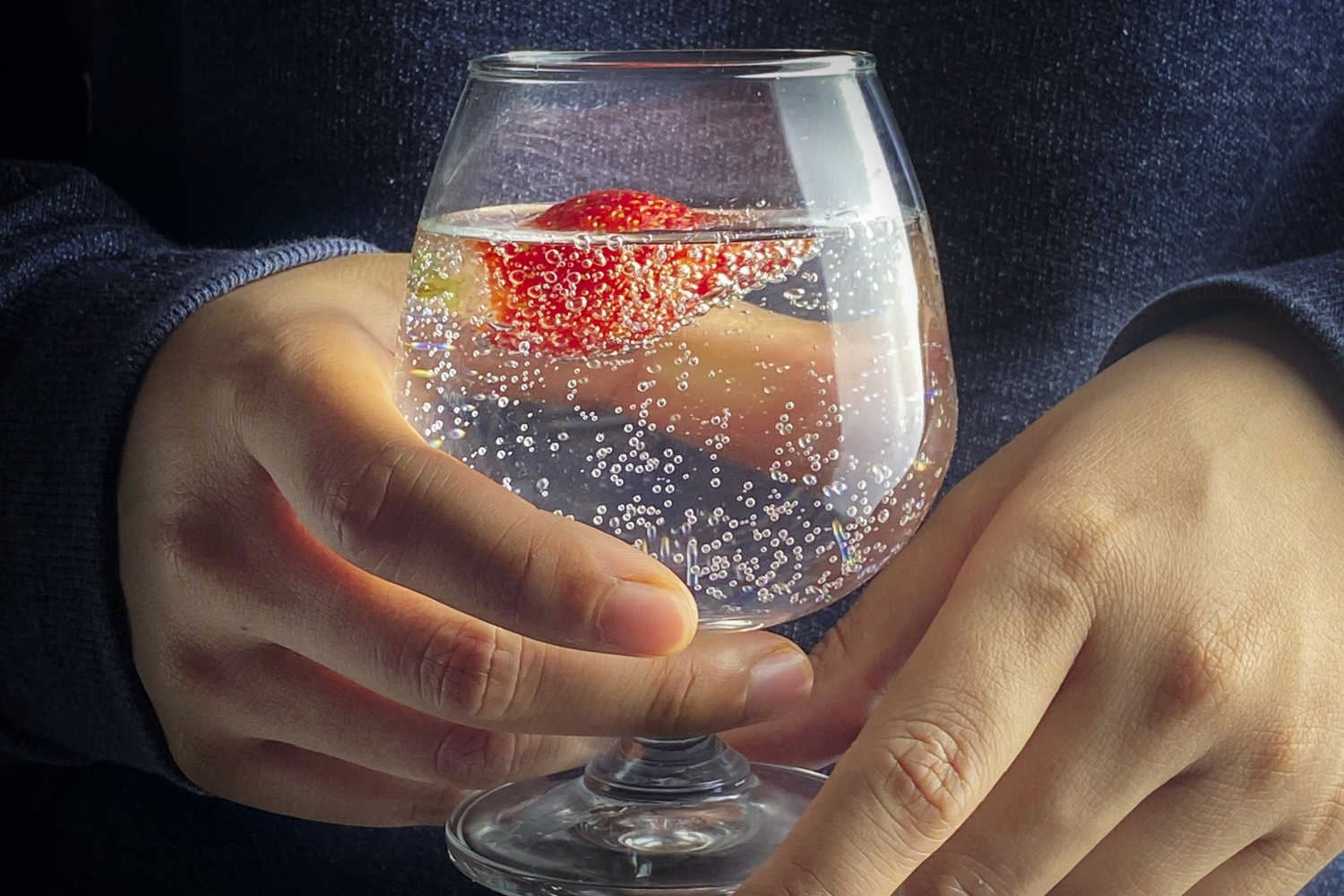 woman holding a glass of sparkling water with a strawberry in it