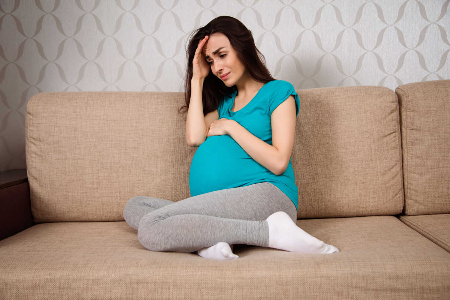 pregnant woman crying sitting on sofa
