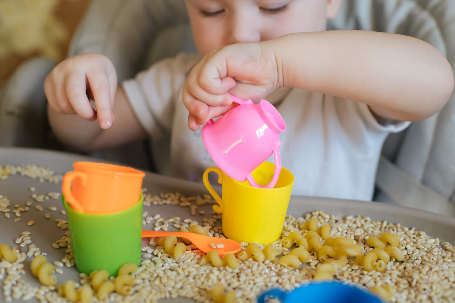 A toddler playing with pulses, grains etc.