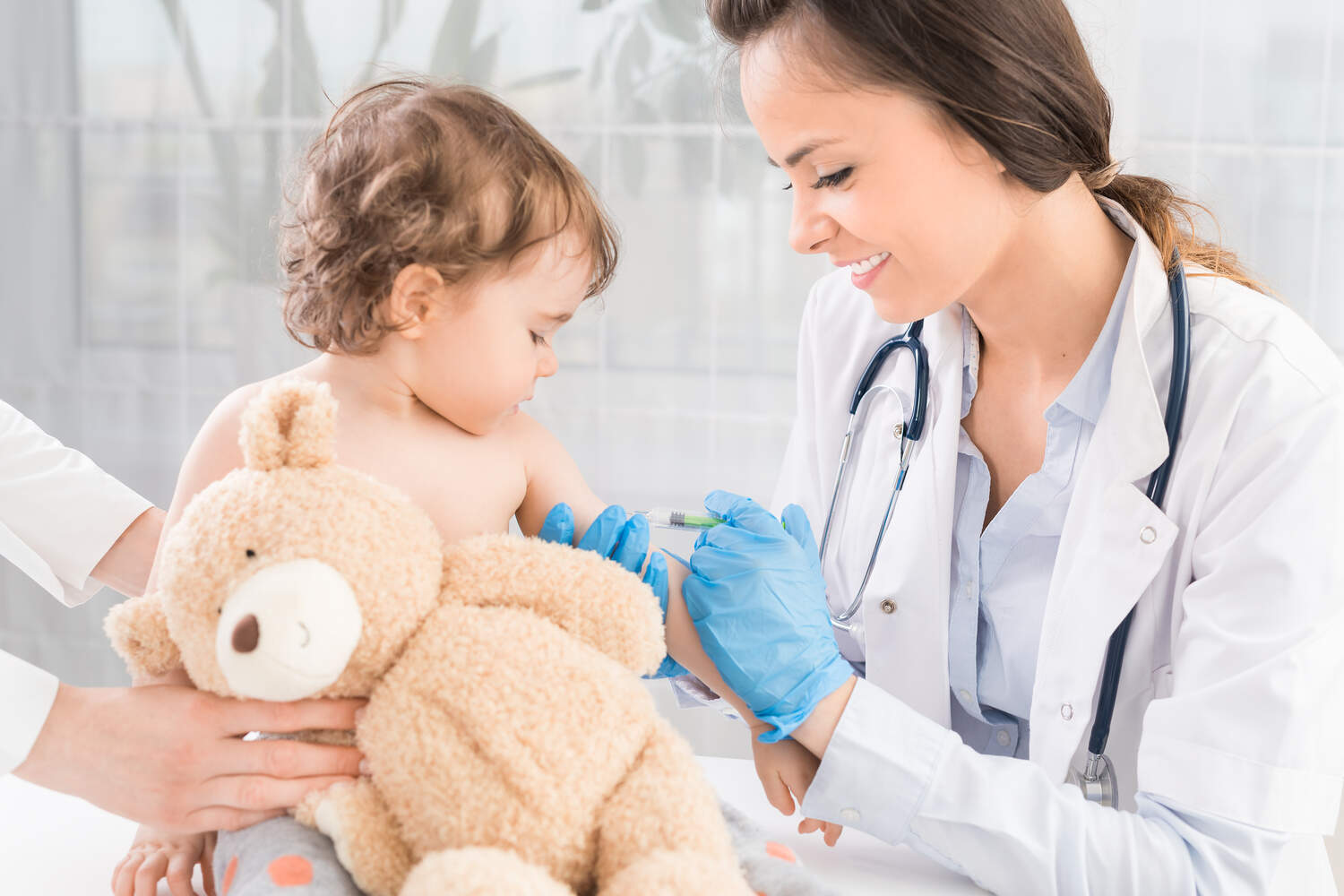 A toddler holding teddy bear and getting injected