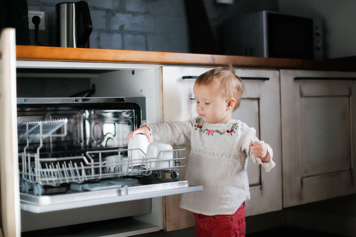 A toddler girl putting glass in dishwasher